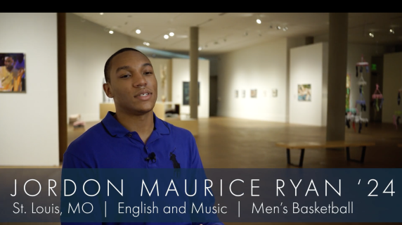 Jordon Maurice Ryan '24, an English and Music major from St. Louis, MO and a member of the Men's Basketball team, speaks to the camera. Behind him are multiple art displays, some from Black artists, from the Grinnell Museum of Art.