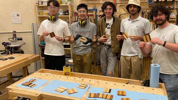 Workshop participants hold the wooden coasters they made in the Makerspace woodshop.