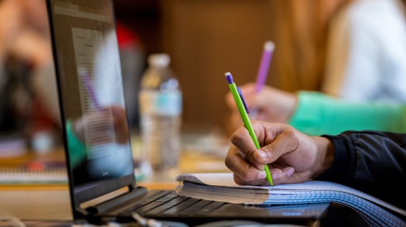 Someone writing on paper with laptop in front of them