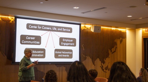 a woman leads a presentation and stands in front of a screen
