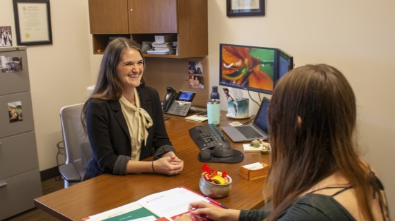 a woman smiles while meeting with a student at her desk