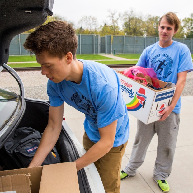 Members of Student Athletes Leading Social Change load donations into the trunk of a car