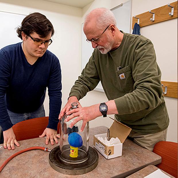 professor and student create a vacuum in a bell jar