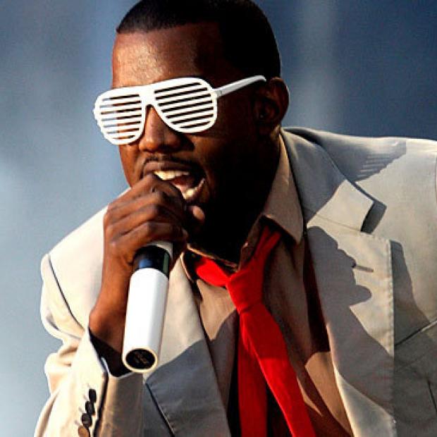 Kanye West in white grill glasses singing at a concert