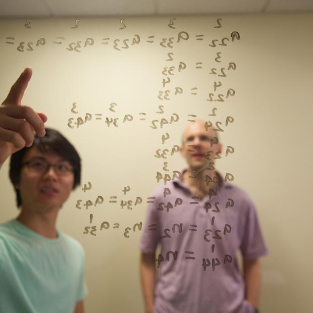 professor and students write equations on markerboard