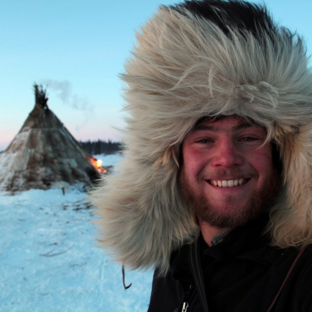 Alex Reich in the Arctic in a fur hood with a teepee structure in the background