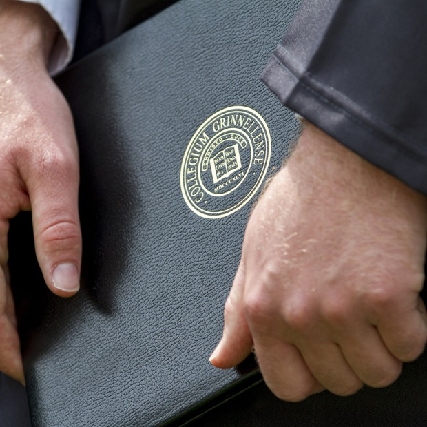 Hands holding diploma case with Grinnell College seal at Commencement