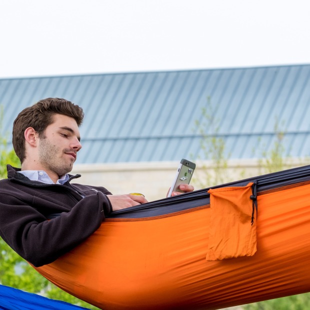 Person on central campus in a hammock holding a cell phone