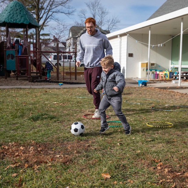 College student playing soccer with preschool student