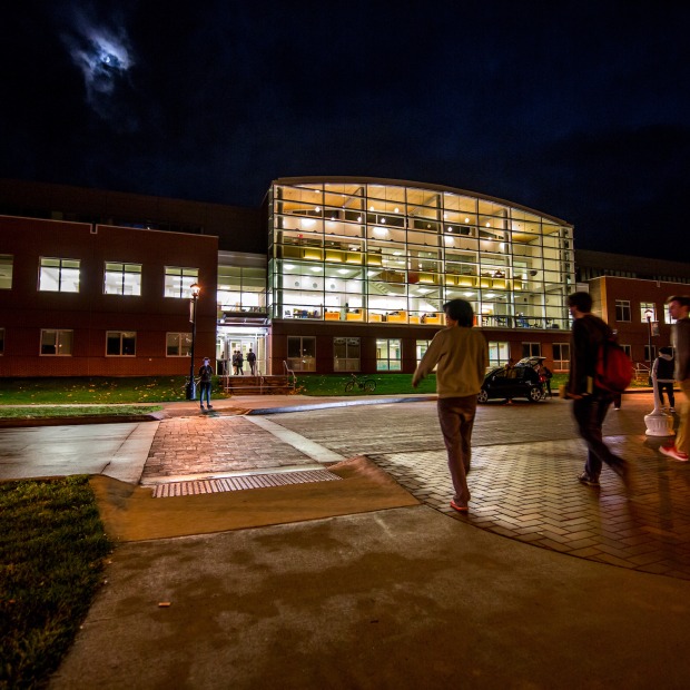 Night time picture of a building with light spilling out as students walk in