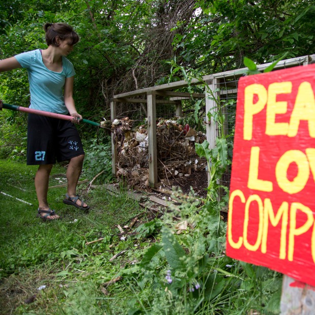 Student adds compost materials to a bin with a red sign that says peace love compost