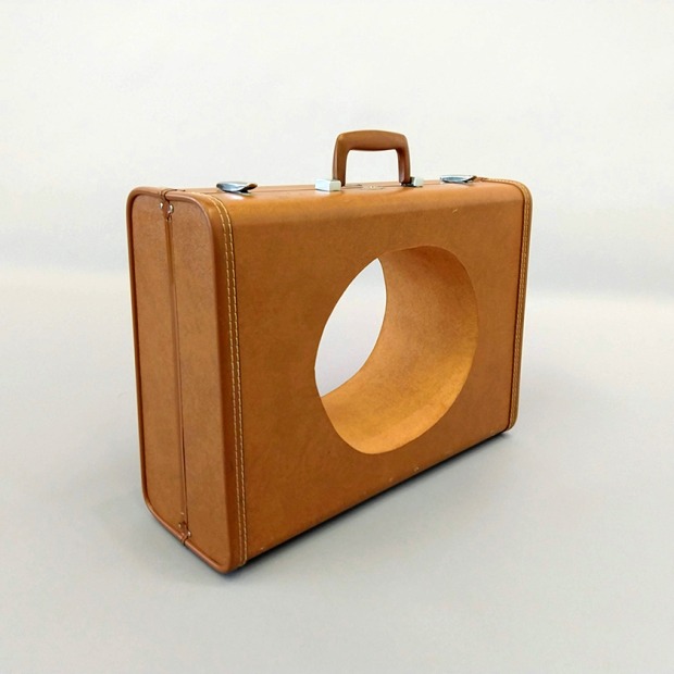A sculpture resembling a light tan suitcase with a large circular hole cut through it
