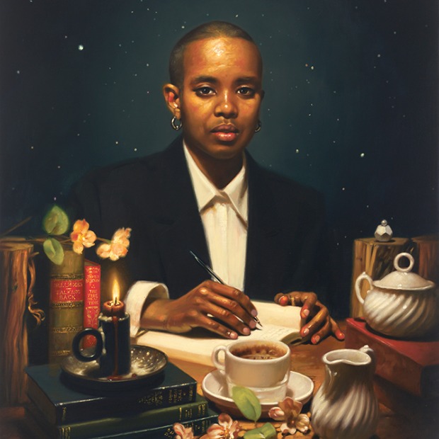 Portrait of curator Nimco Kulmiye Hussein seated at a table writing a letter, staring directly at the viewer, with books, a cup of coffee, and other objects arranged on the table she is seated at.