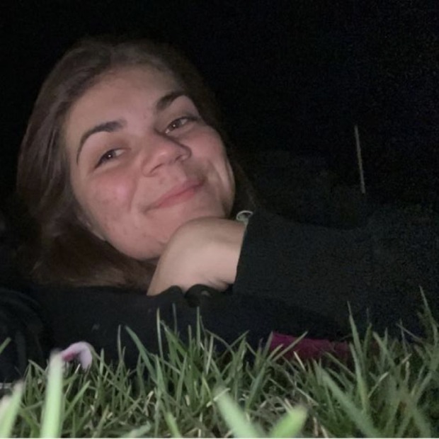 Anastasia Rompi smiling at the viewer, laying in grass at night