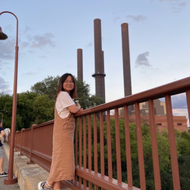 Jinglin Xiong, standing on a ledge with an red iron fence and smokestacks in the background
