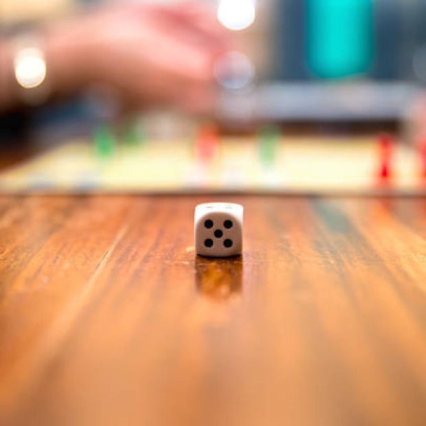 A six-sided die rests on a table. The background is fuzzy with playful colors.
