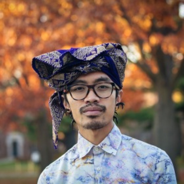 Putu: standing in front of an autumnal background, relaxed expression, goatee, glasses, wearing patterned shirt and Balinese udeng.