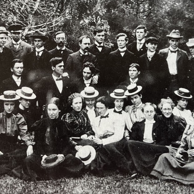 blank and white photo of students outside, the men in suits and the women in long dresses and boaters