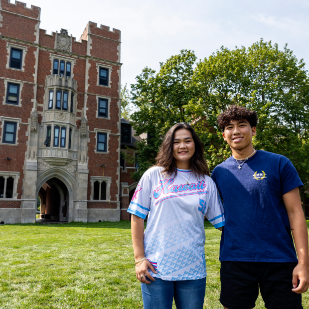 Kylie Ann Smith '27 and Preston Yoshida '27 stand in a green Mac Field in front of a looming Gates Tower.