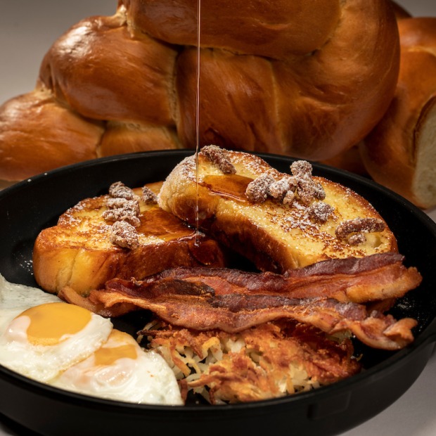eggs, bacon, hashbrowns and french toast in a dish. a loaf of sweet bread sits behind the dish