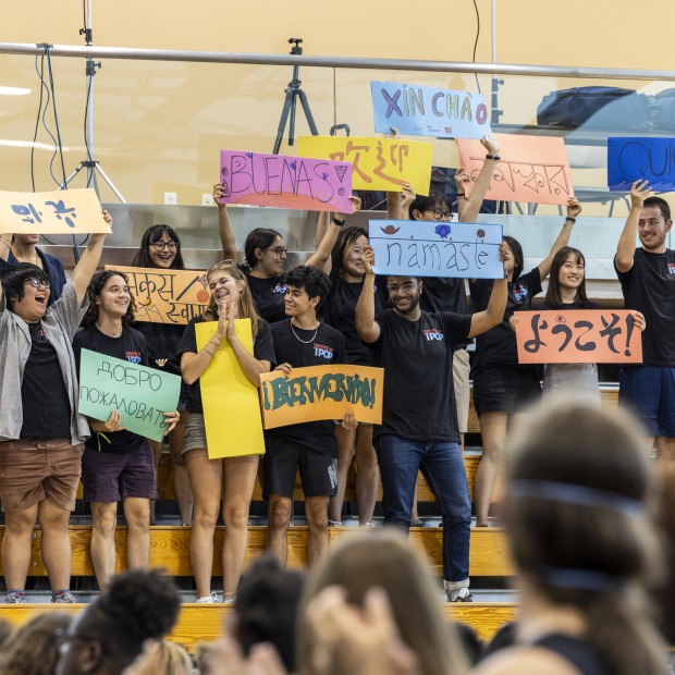 international college students standing in a gymnasium hold up signs in various languages