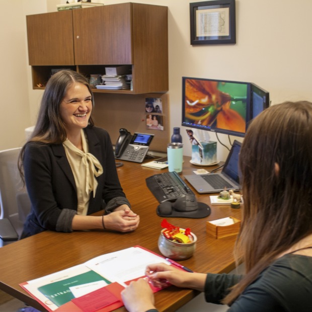 a woman smiles while meeting with a student at her desk