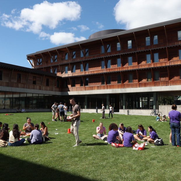 Students stand and sit in small circles in the grassy courtyard of Renfrow Hall.