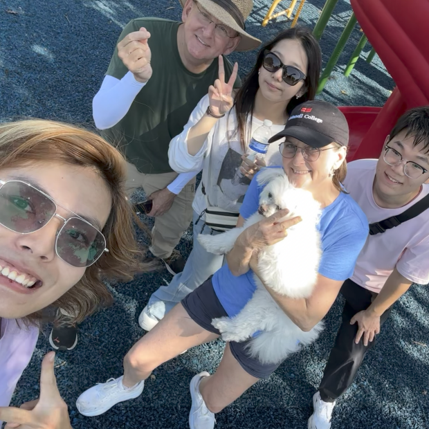 A group of people stand in front of a red slide outside and smile at the viewer.