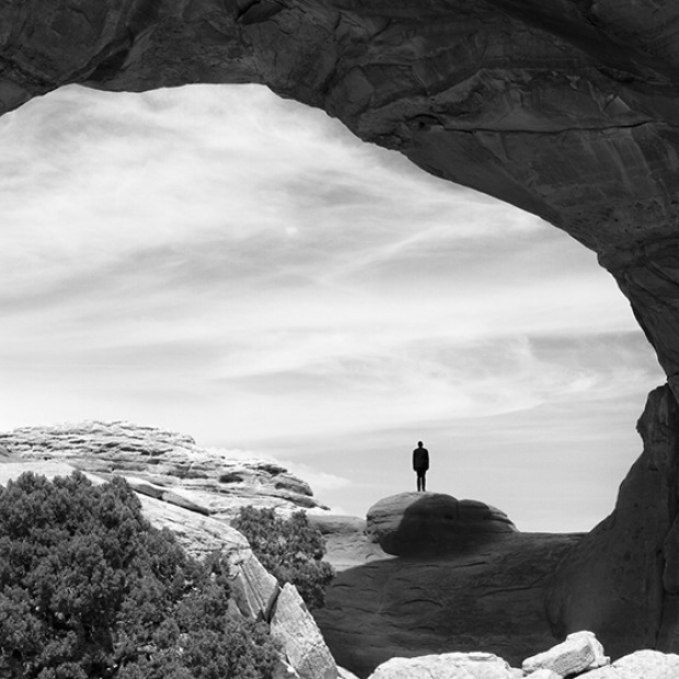 Photograph by Johnnie Chatman looking out from a cave toward a man standing on a rock, with his back to the viewer.