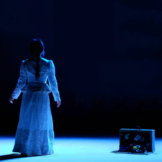 performer bathed in blue light approaches darkness.