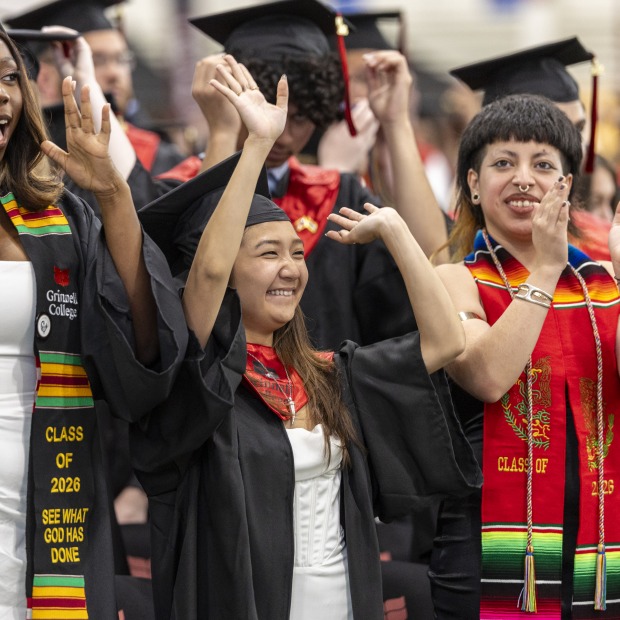 Students wearing black graduation gowns and caps standing and applauding