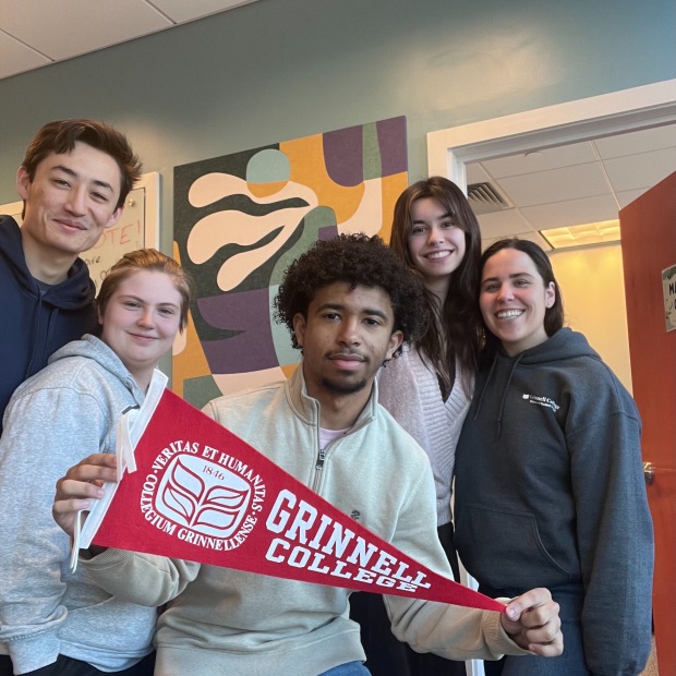 5 Grinnell students smile for the camera, one of them holding a pennant that says "Grinnell College" on it