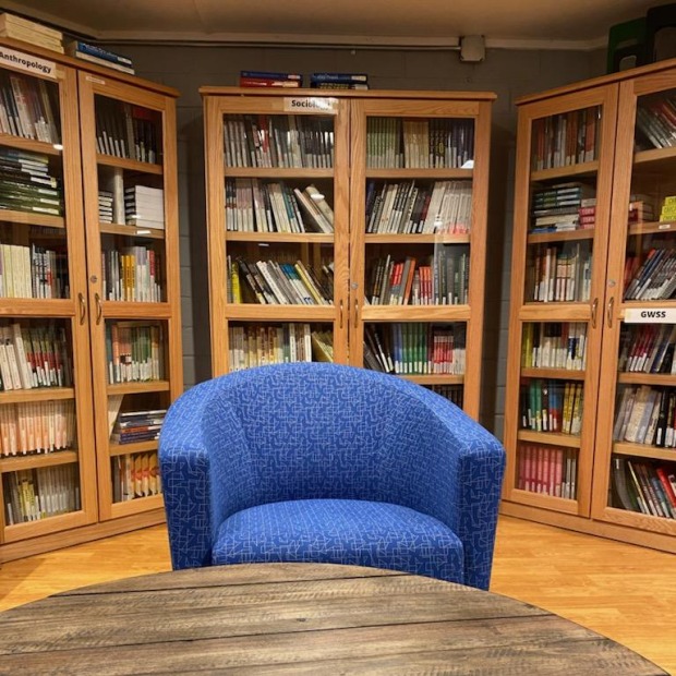 Behind a table and armchair are shelves filled with textbooks