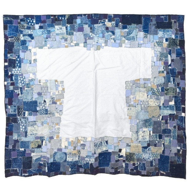 An image of a taprestry that has a flat white tee shirt in the center, surrounded by abstracted small squares of blue fabric.