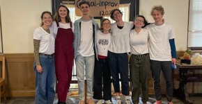 Seven people in casual clothes stand in front of a double-door displaying a cardboard sign that includes the words venmo and improve