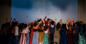 Performers on stage in various traditional dress against a starlit backdrop