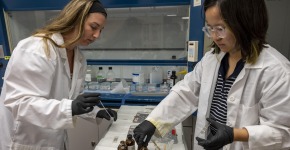 Two students in lab coats work on their research.