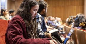 A student in a lecture hall takes notes on her laptop.