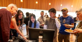 A small crowd looks very engaged as they watch a woman presenting. In the background are many others.