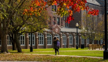 Student walks on campus with colorful leaves in the fall