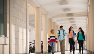 Four students walk down the loggia hallway outside of their dorm