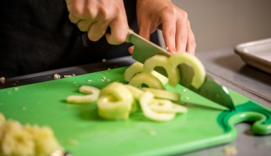 A close-up of hands chopping up vegetables with a knife.