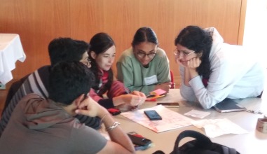 A group of five students huddles at a round table to develop their project idea. 