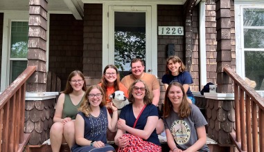 MJ Uzzi and Professor Deborah Michaels pose with friends and a dog on the porch of a house