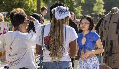 A student with glasses and a blue shirt talks to two students outdoors.