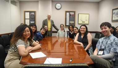 Nine students sit around a conference table with an older gentleman, Senator Chuck Grassley standing at the head.