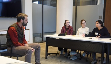 Three students sit at table opposite Cory Turner '98