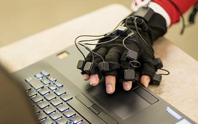 Hand in motion-capture glove hovers over the touchpad of a laptop computer 