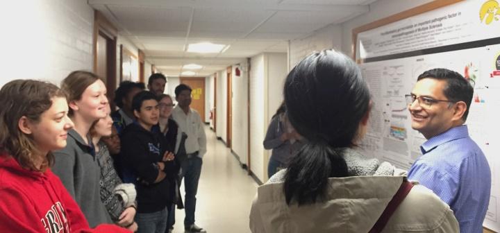 Ashutosh Mangalam talks about a research poster with students of Biology-395 Immunology in a corridor outside his laboratory.