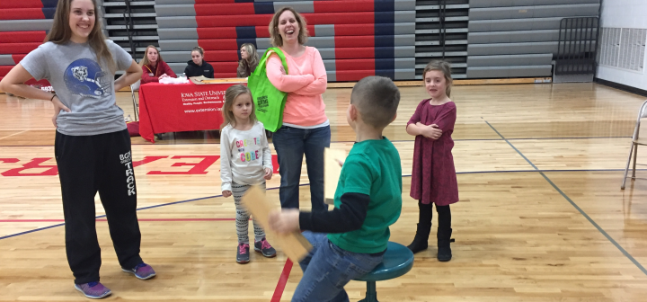 A child's family laughs while he spins on a stool to feel the effects of conservation of angular momentum.